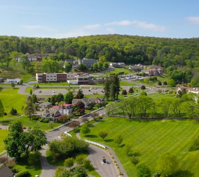 An overhead drone image above Caron Pennsylvania's campus, with rolling green hills and buildings in the distance.