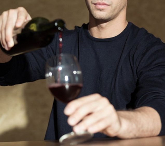 Person with their face cropped out pouring red wine into a wine glass.