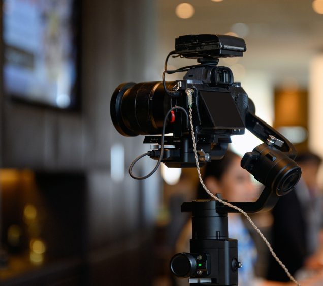 Press conference with digital camera facing a stage that has a bokeh effect.