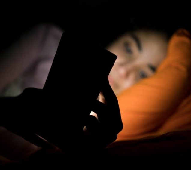 Person laying in bed in the dark, the light from their phone screen shining on their face.