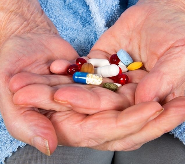 Hands of an older individual holding a colorful smattering of pills.