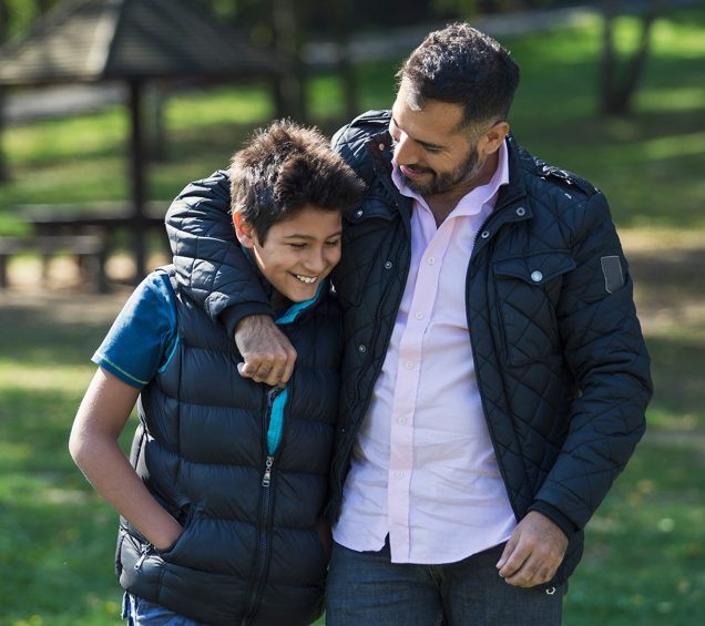 Father with arm around his son while walking in a green grass park.