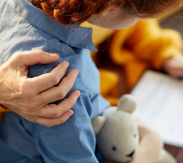 Close Up on woman's hand comforting a child's shoulders while holding a teddy bear.
