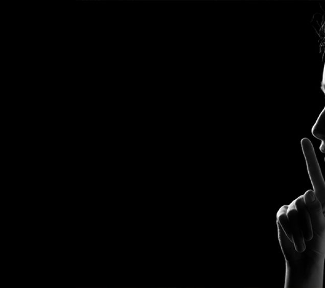 Profile of a person with their index finger over their mouth against a black background.