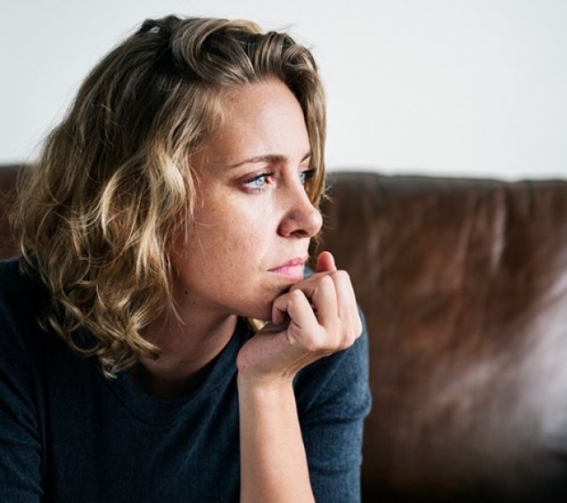 Woman sitting on a couch with her chin in her hand looking off thoughtfully.