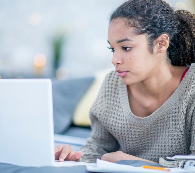 Teenage girl on white computer while sitting outside.
