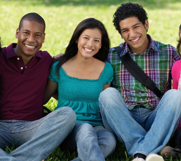 5 Diverse teenagers sitting on the lawn while smiling.