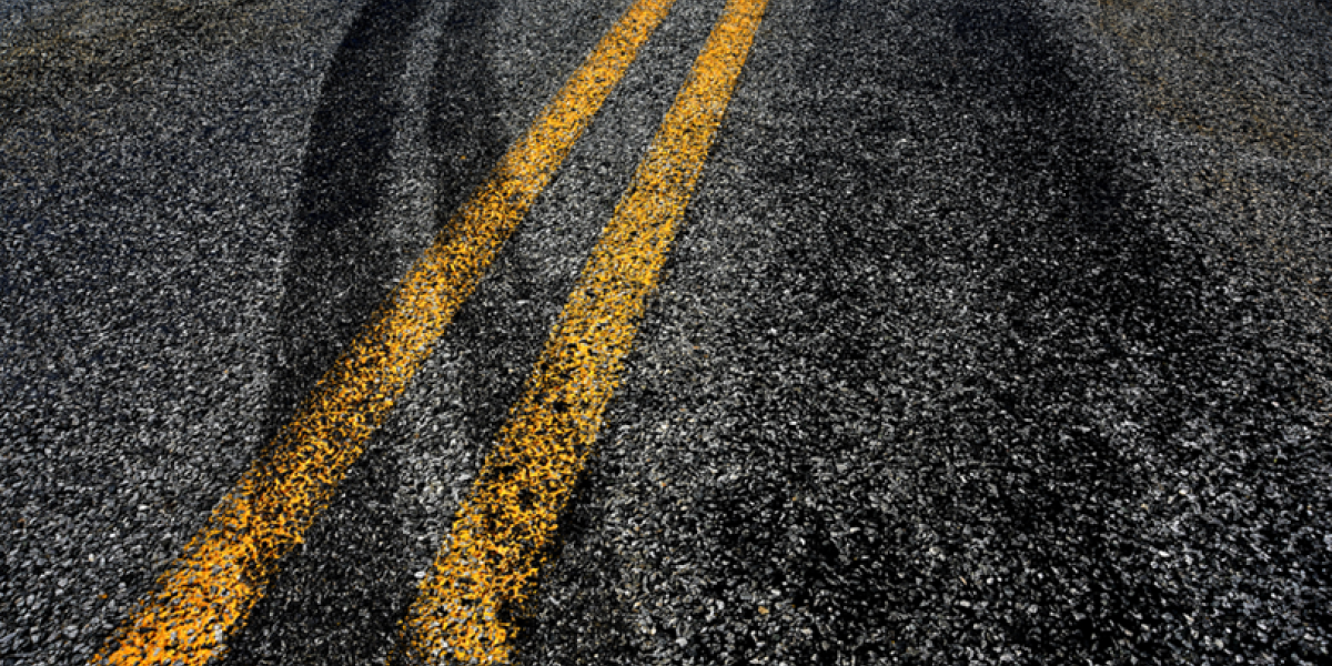 Close up of asphalt with tire tracks crossing the lane dividing lines.