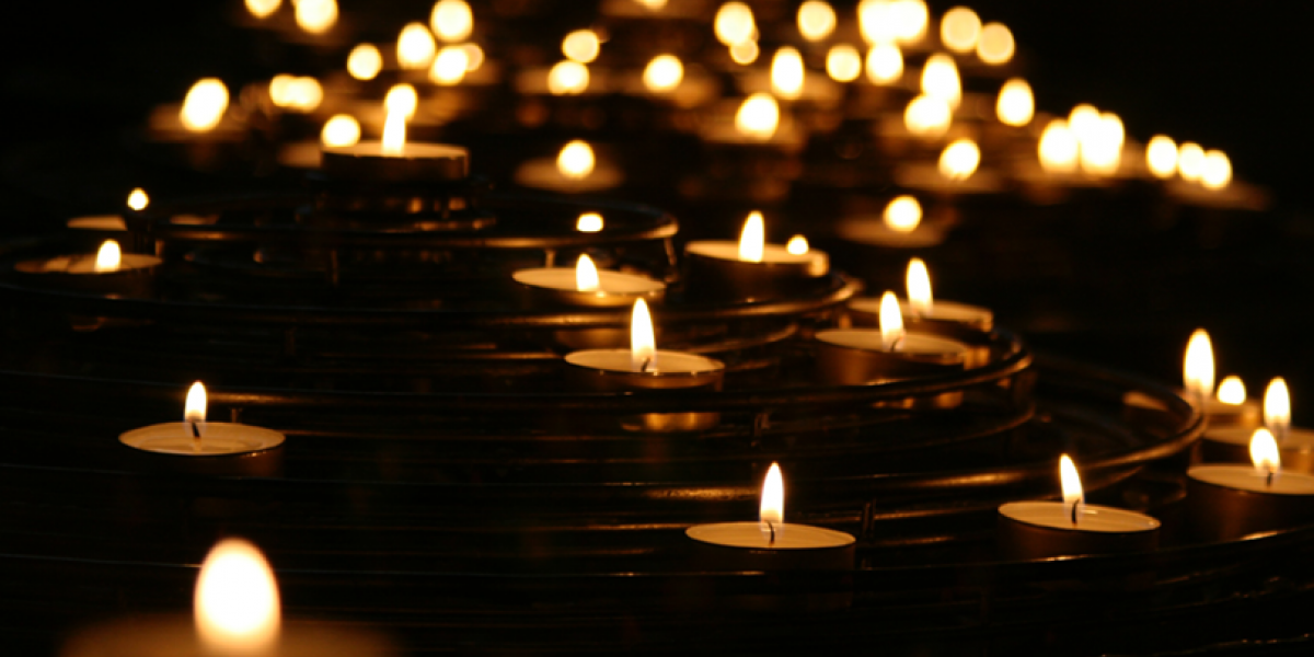 Many flames of votive candles lit in darkness.