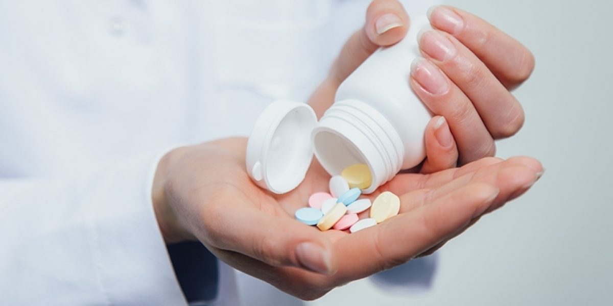 Hands dumping pills out of a pill bottle.