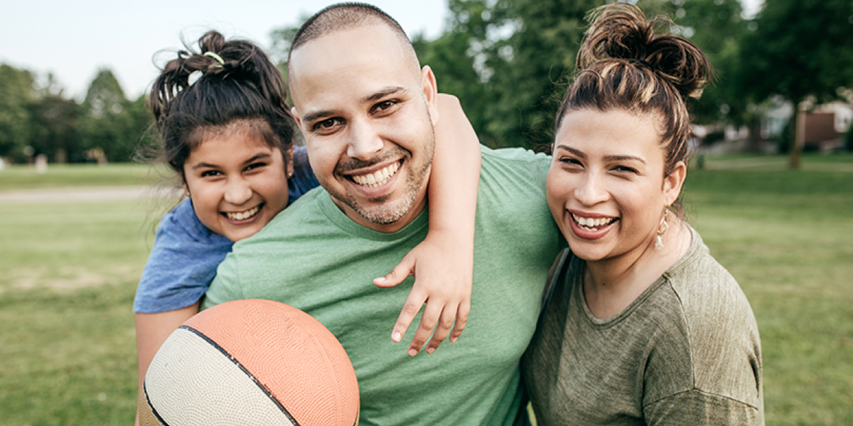 Mom, Dad and young daughter smiling at the camera, holding a basketball.