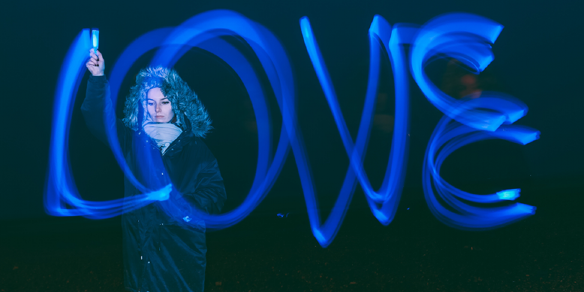Woman in parka using a blue light to write out the word love in the dark.