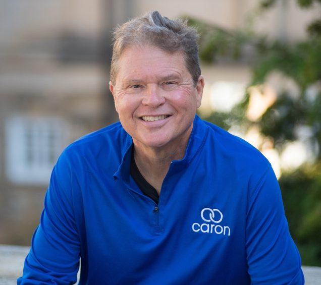 Smiling man in a blue shirt with a Caron logo.