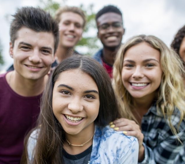 Group of six teen boys and girls in a group smiling for the camera.