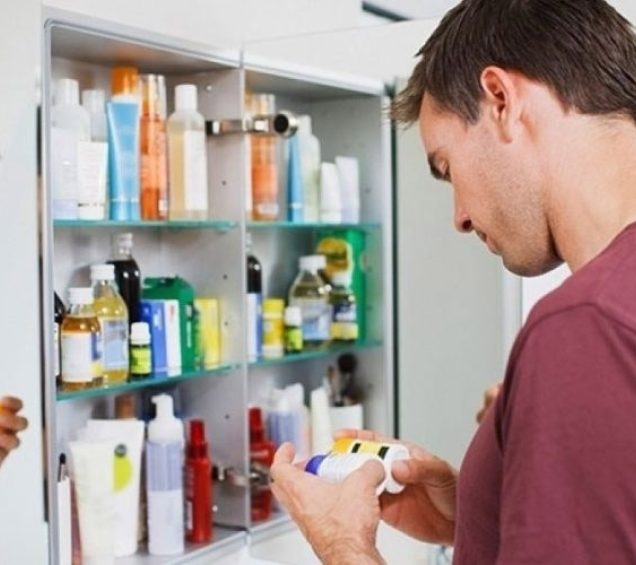 Man standing at his medicine cabinet looking at the labels of the medicine bottles.