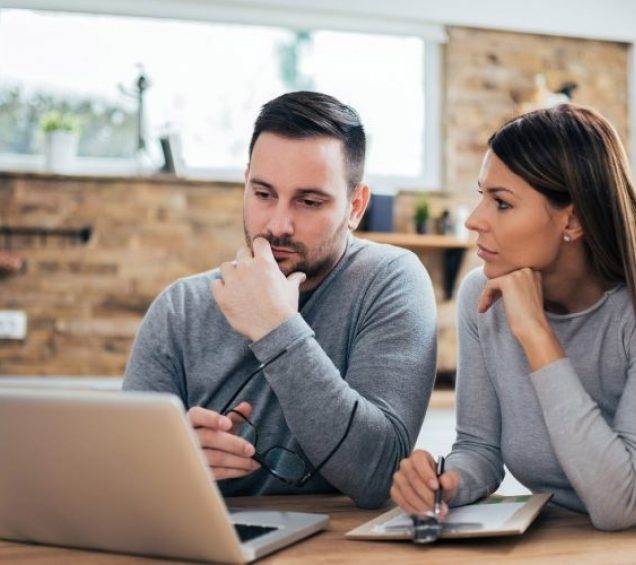 Man and woman at home looking at a the screen of a laptop on a desk.