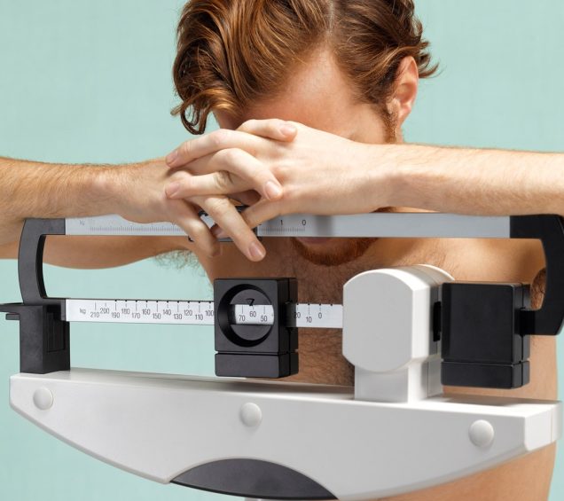 Man standing on a scale footing down at his feet with his arms over the top of the scale.