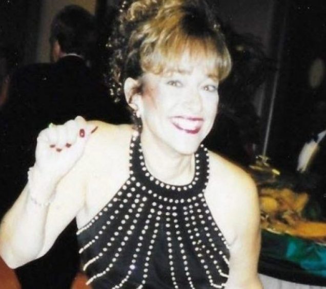 A woman in a black dress at a banquet dinner smiling and waving.