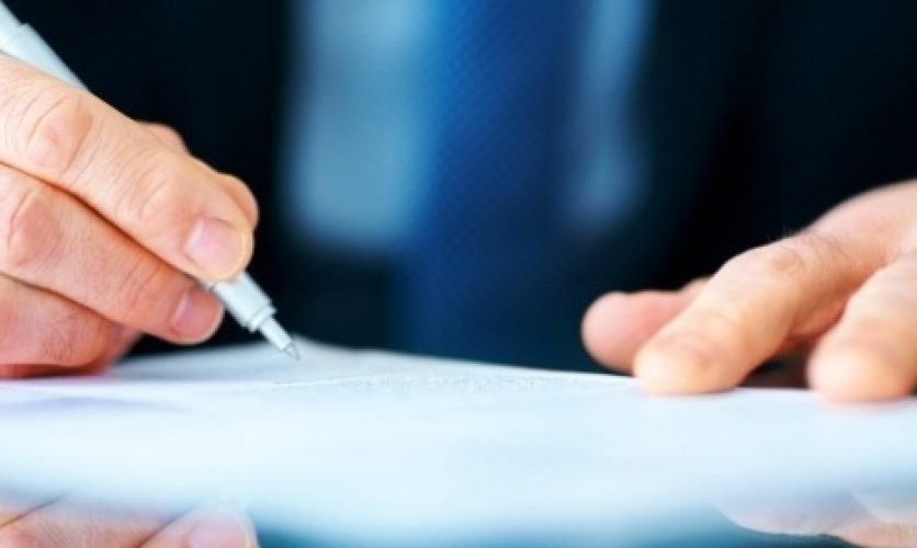 Hand holding a pen and signing a document.