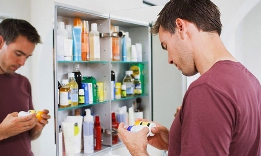 Man standing at his medicine cabinet looking at the labels of the medicine bottles.