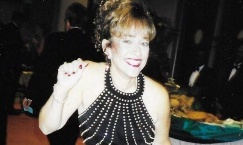 A woman in a black dress at a banquet dinner smiling and waving.