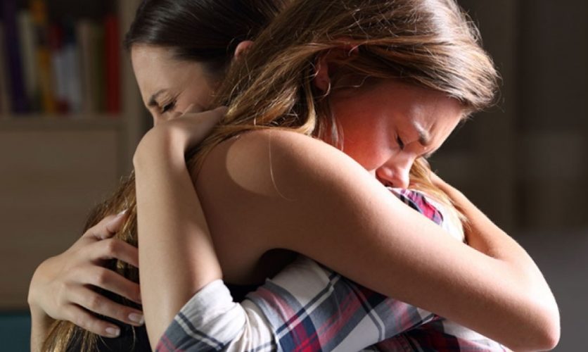 A child and their parent tightly embracing and looking distraught.